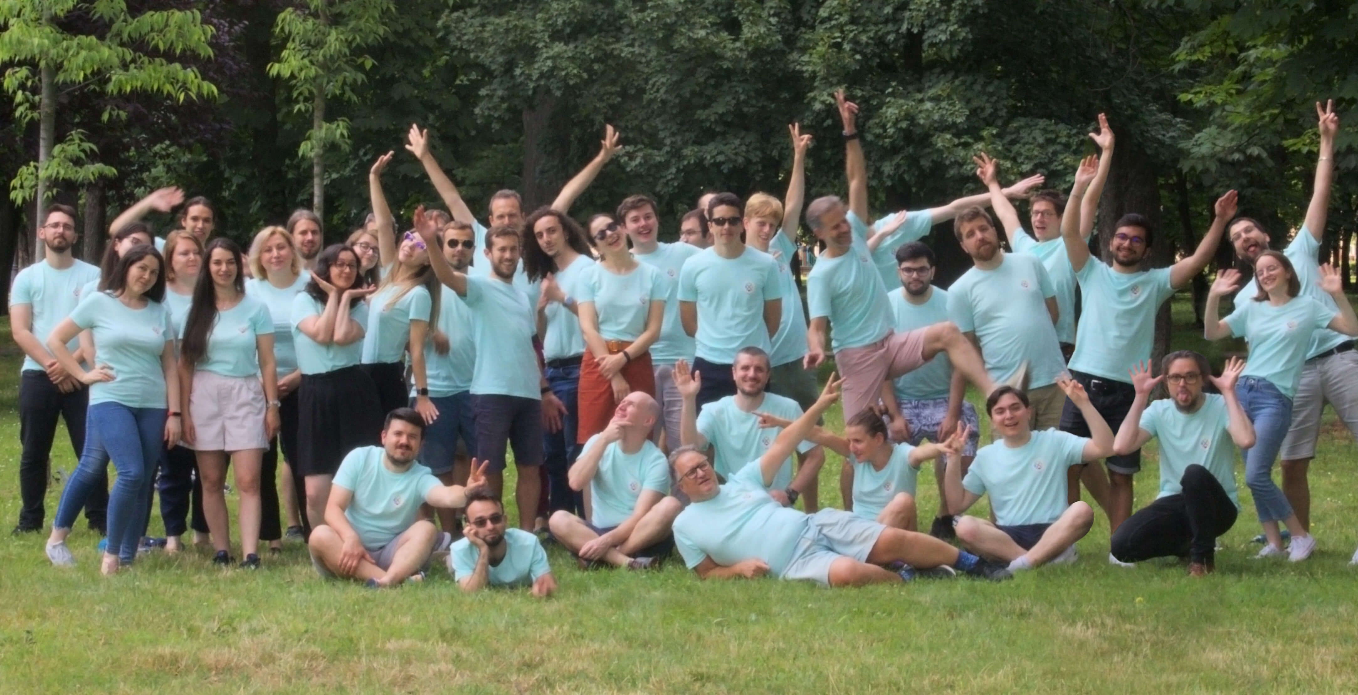 A large group of joyful people in light blue shirts celebrating outdoors on grass.
