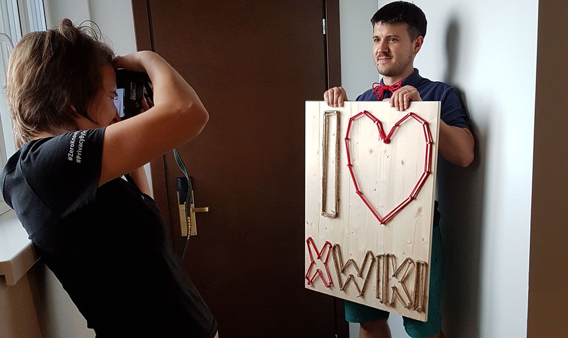 Person photographing another person holding an 'I love MWIKI' string art sign.