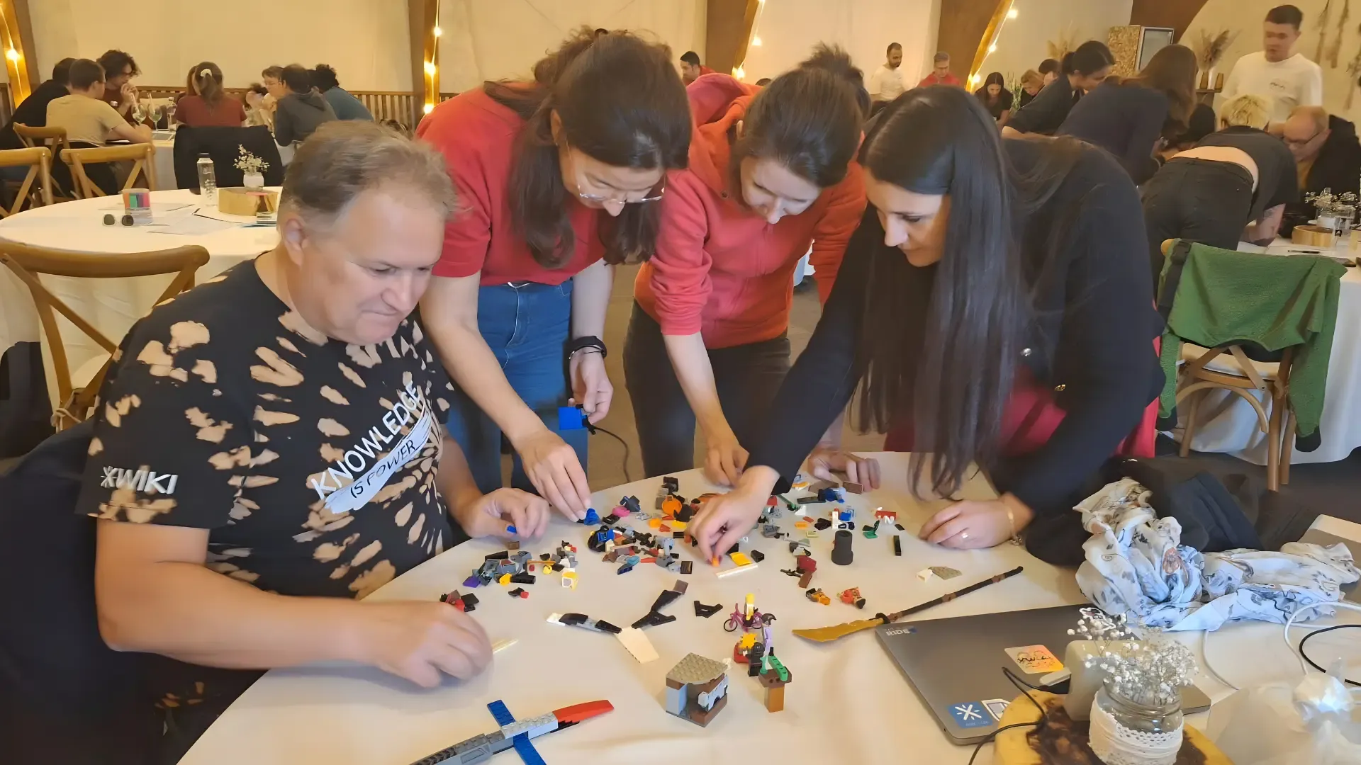 Four people collaborate intently, building with colorful LEGO blocks on a white table.